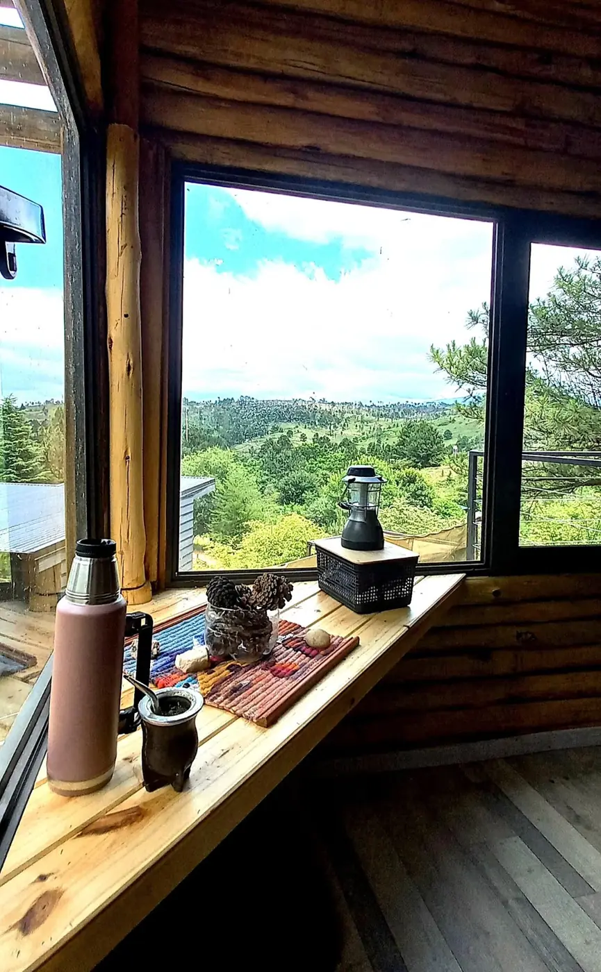 Vista de las sierras desde el ventanal de una cabaña en Intiyaco, con mate y termo
