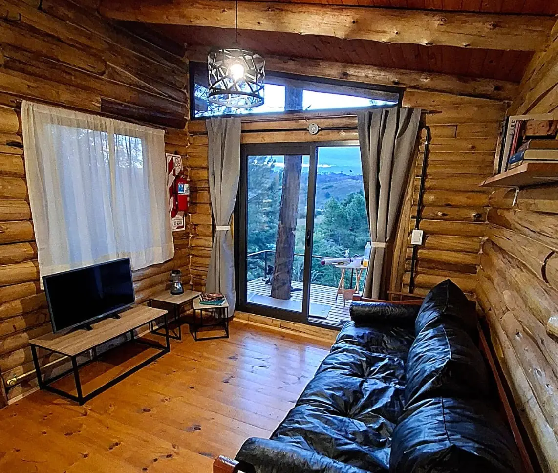 Living de la cabaña para parejas con ventanales al bosque